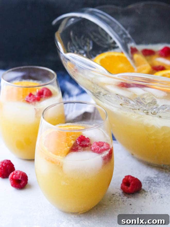 A serving of Mimosa Punch in a champagne flute, garnished with a fresh raspberry, taken from the vibrant punch bowl on a rustic wooden table.