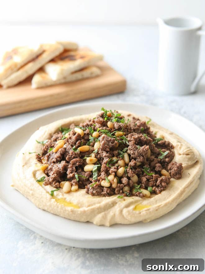 A close-up view of the appetizing hummus dish, generously topped with savory spiced ground beef and crunchy pine nuts, ready to be enjoyed with warm pita bread.