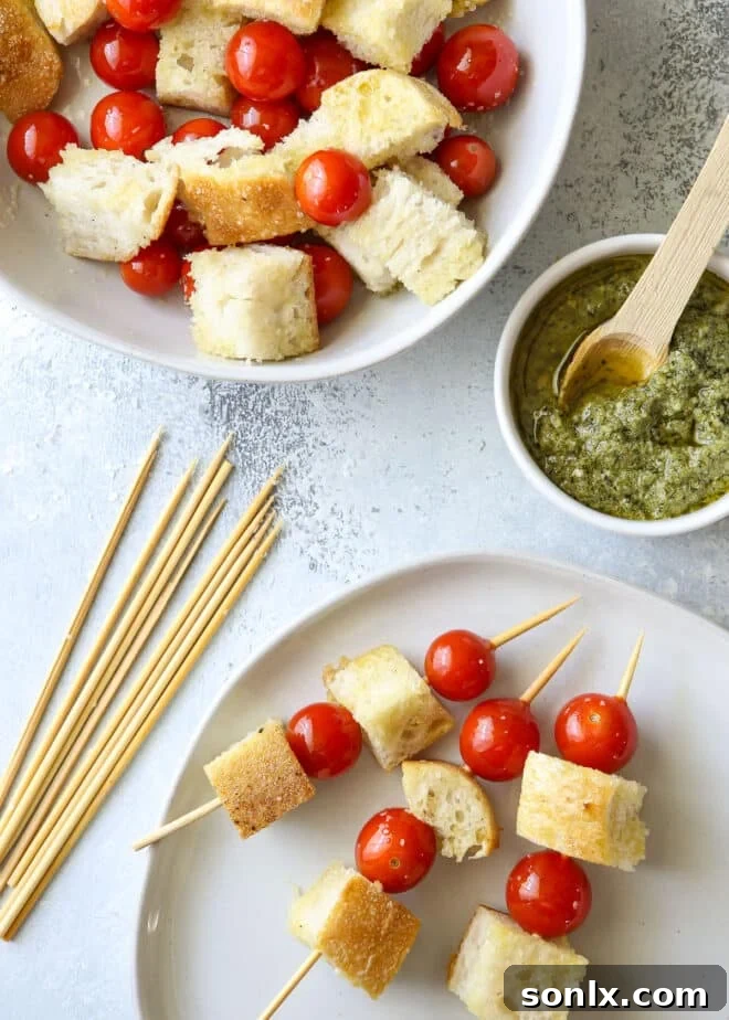 Hands demonstrating the assembly process of grilled bruschetta skewers, alternating cubes of bread and whole cherry tomatoes on bamboo skewers.