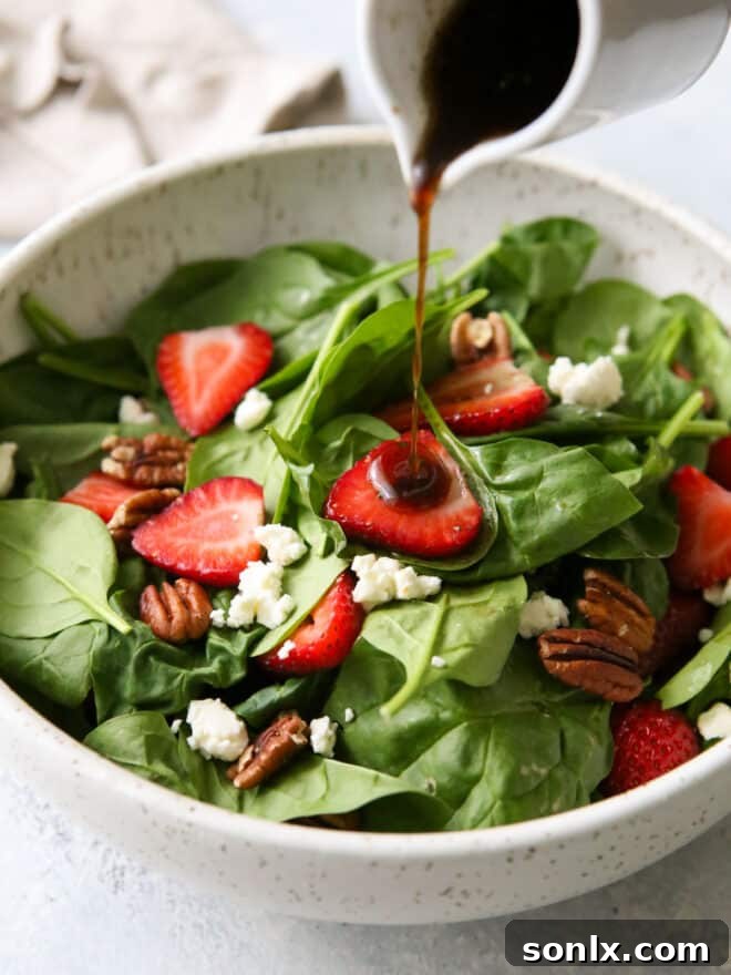 Warm brown butter balsamic dressing being poured over a fresh strawberry spinach salad, highlighting its rich color and texture.