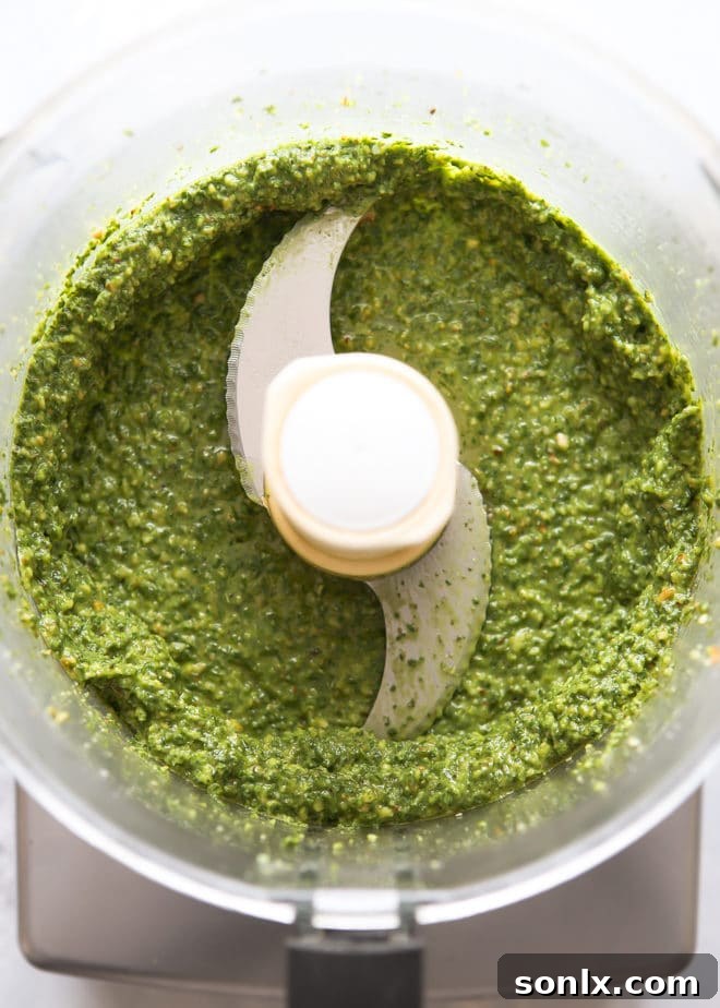 Adding olive oil to basil walnut pesto in a food processor