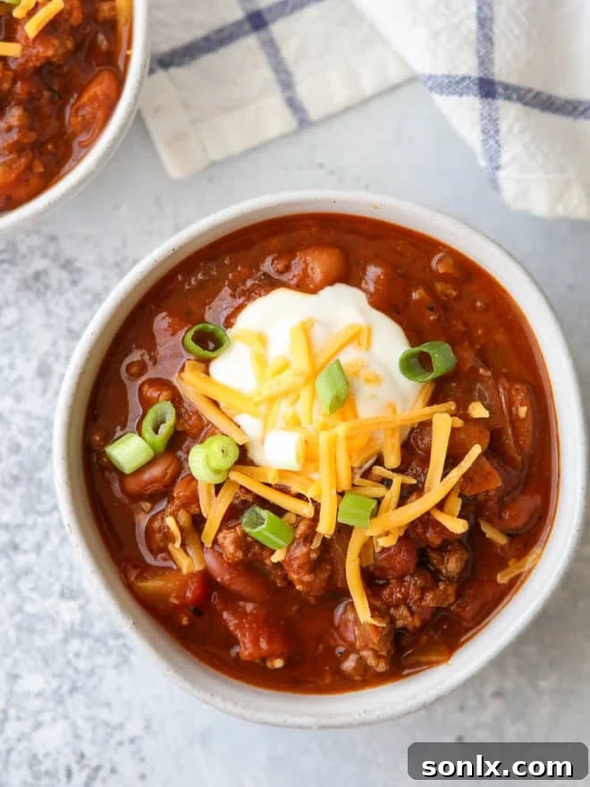 closeup of a bowl of chili with sour cream, cheese and green onions