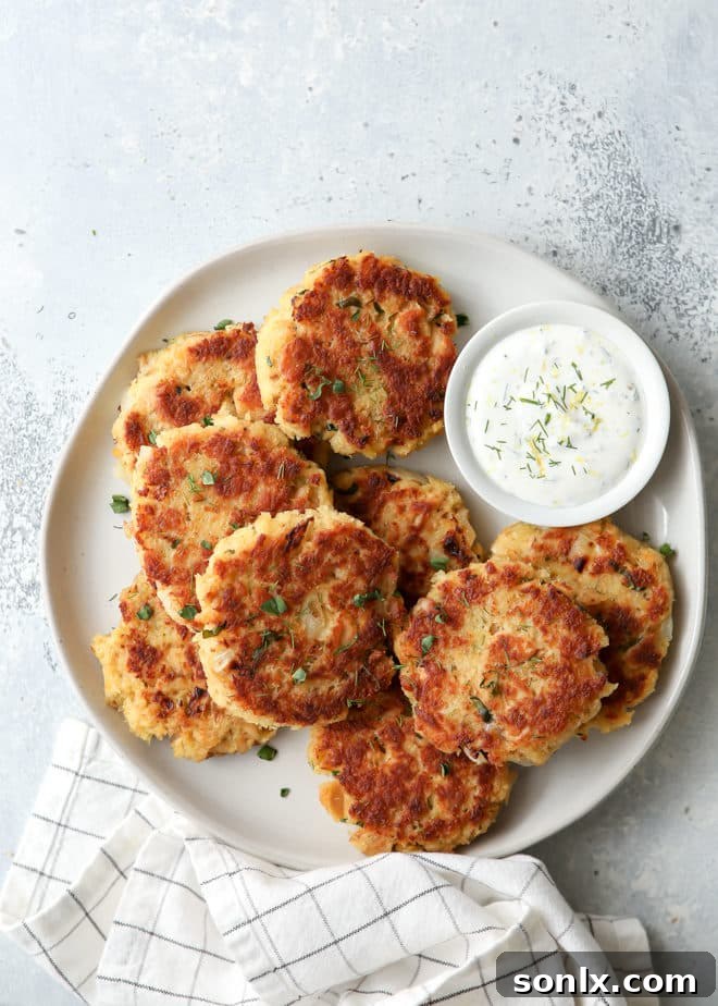 A beautifully plated salmon patty served with a creamy green herb sauce and a fresh lemon wedge.