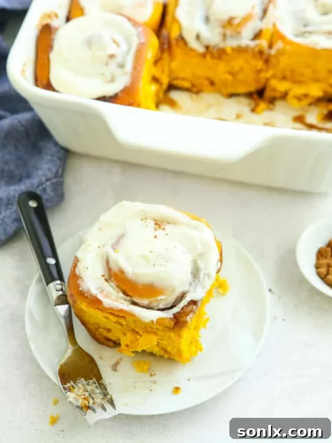 a single pumpkin cinnamon roll on a white plate with maple icing