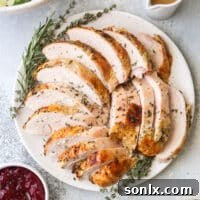 Sliced herb-roasted turkey breast on a platter alongside a salad, cranberry sauce, gravy, and rolls, ready to be served.