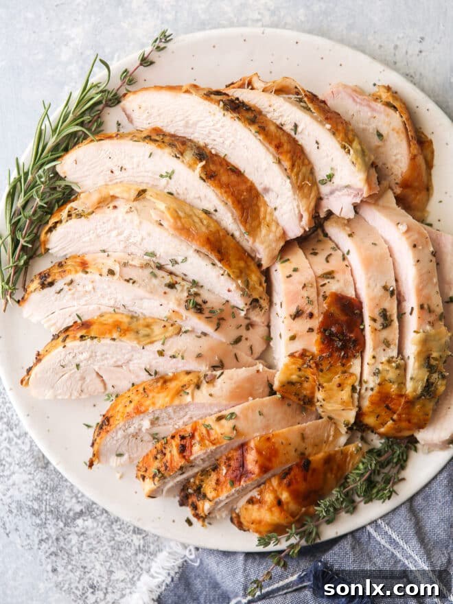 Close-up of moist, sliced herb-roasted turkey breast garnished with fresh herbs on a pristine white plate.