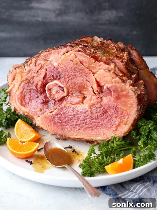 A beautifully glazed spiral ham garnished with fresh orange slices and herbs, ready to be served at a festive gathering.
