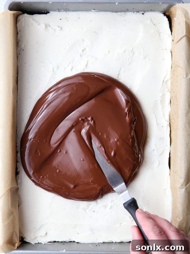 Spreading melted dark chocolate topping evenly over the creamy peppermint layer on the cookie bars.