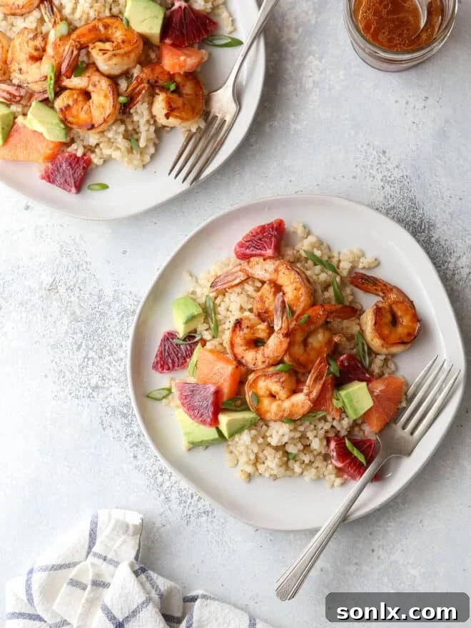 Close-up of citrus shrimp bowls, showcasing the fresh oranges, green avocado, and green scallions on rice.