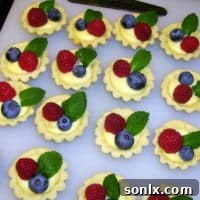 A delightful display of mini lemon curd tarts, garnished with vibrant fresh berries and delicate mint leaves.