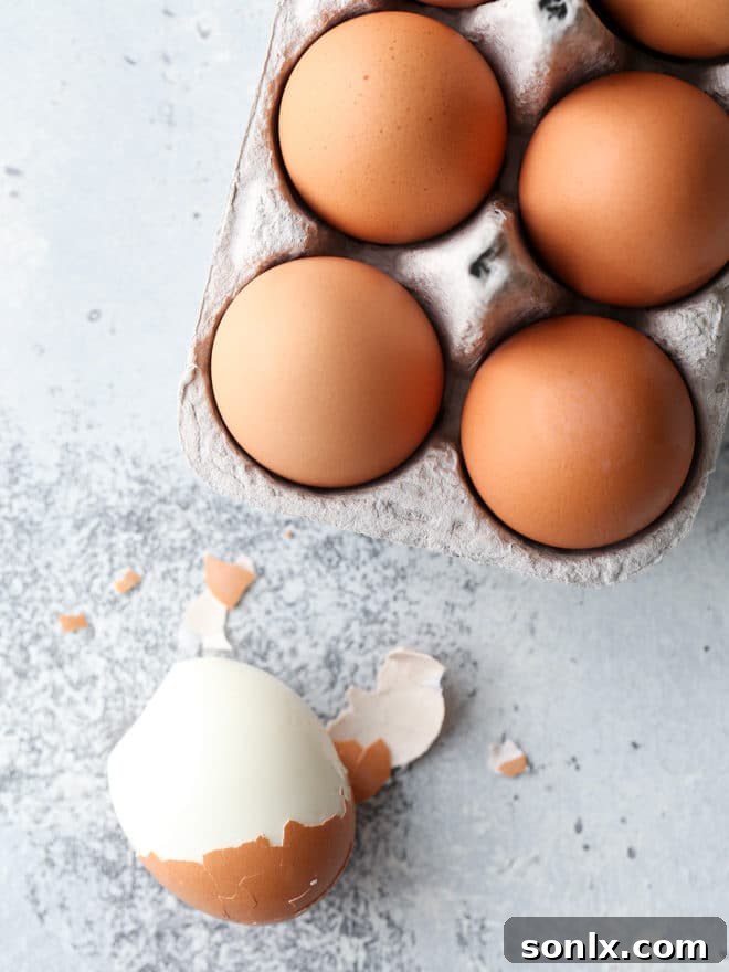 A close-up of a hand gently peeling a perfectly cooked hard-boiled egg, revealing the smooth white underneath, a crucial step in preparing the best deviled eggs.