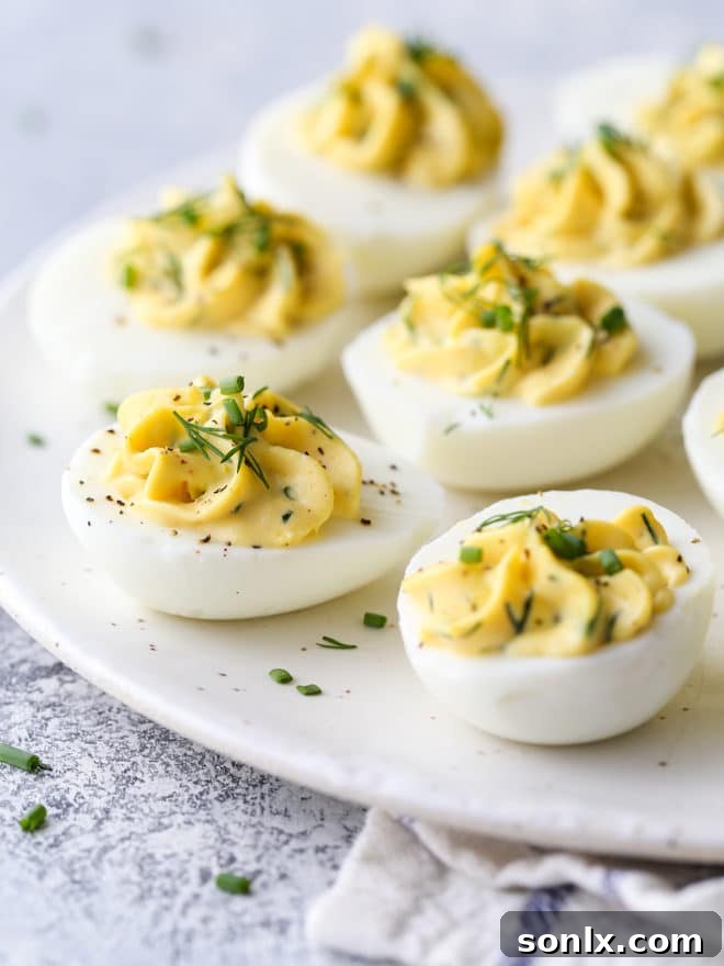 A close-up of classic deviled eggs, artfully arranged and garnished with fresh herbs, ready for a party. The creamy filling is perfectly piped into the egg whites.