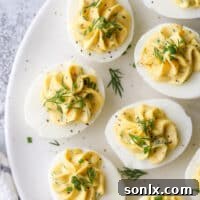 A top-down view of classic deviled eggs, beautifully arranged on a white platter, garnished with fresh herbs, showcasing their creamy texture and inviting appeal.