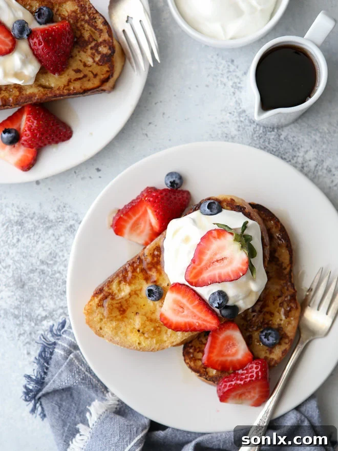 Thick, golden-brown slices of French toast piled high with fresh berries and whipped cream, ready to be drizzled with maple syrup.