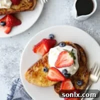 A stack of golden French toast slices, garnished with fresh berries and whipped cream.