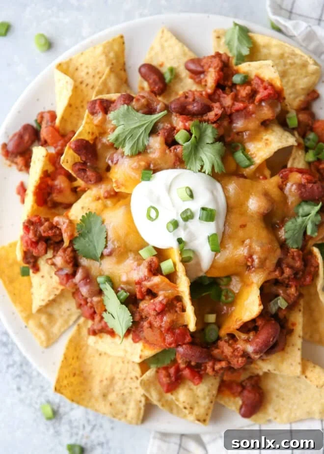Closeup of a plate of vibrant chili cheese nachos, showcasing melted cheese, chili, and fresh toppings.