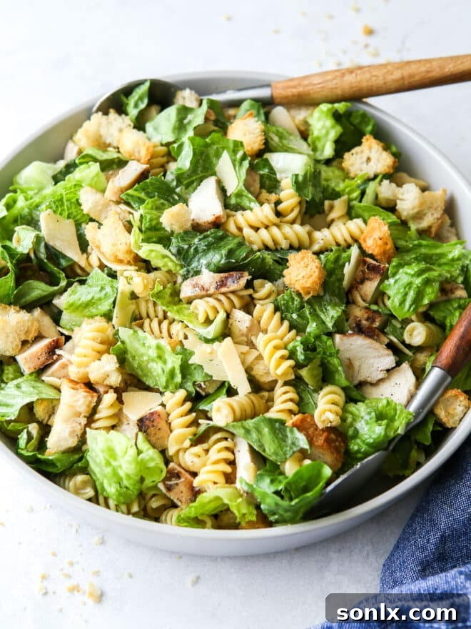 Chicken Caesar pasta salad served in a large bowl with tongs.