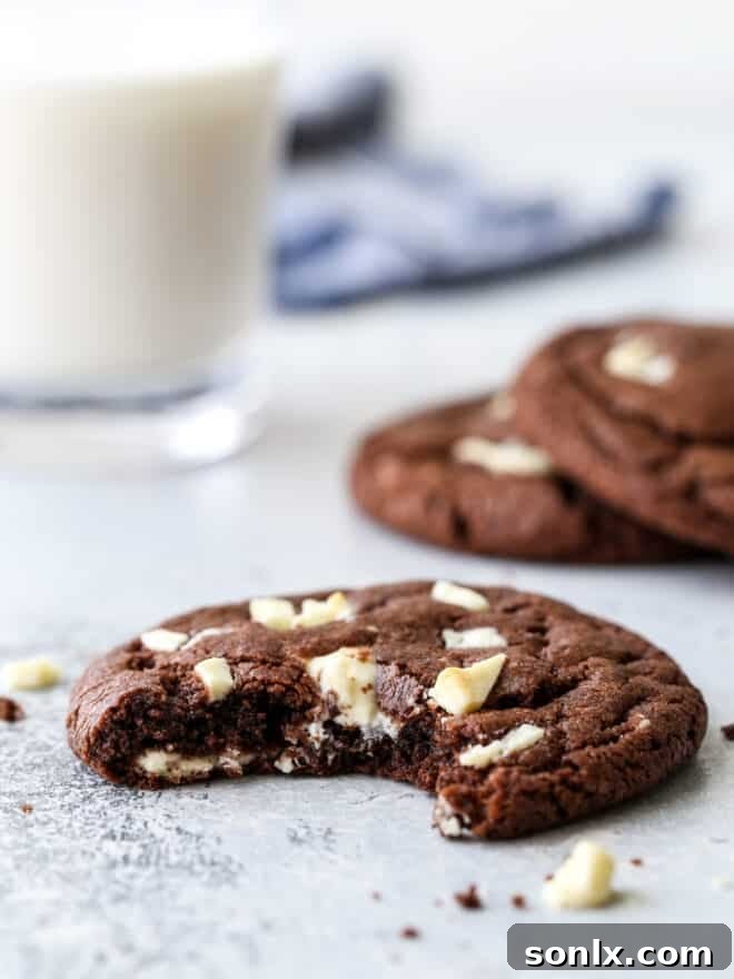 Close-up of a chocolate cookie with white chocolate chips, milk in the soft-focused background, emphasizing its tempting texture.
