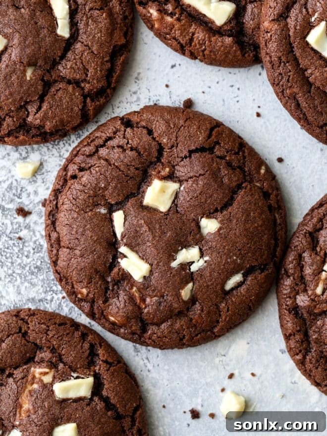 A stack of warm chocolate cookies with white chocolate chunks, invitingly placed on a white surface.