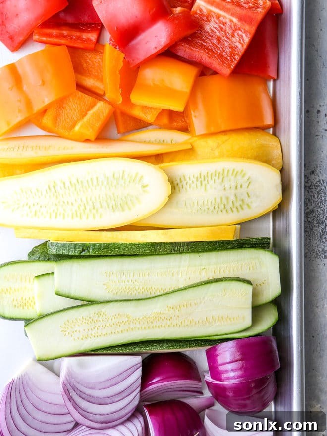 A close-up shot of the fresh ingredients for a grilled vegetable antipasto platter, showcasing colorful bell peppers, zucchini, red onion, Kalamata olives, and crumbled goat cheese.