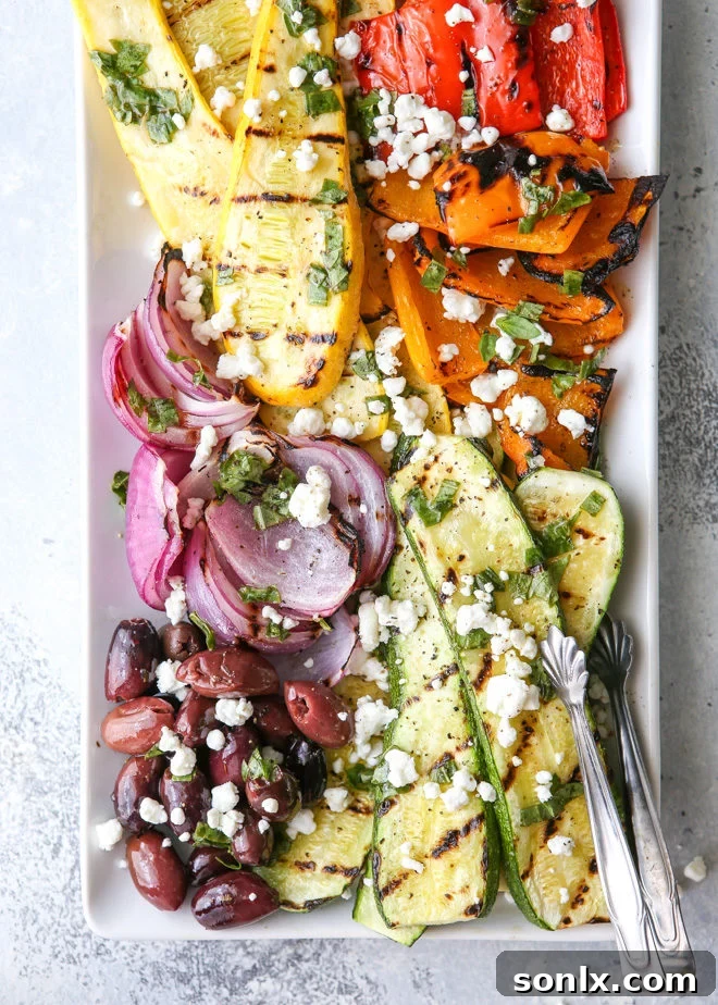 Beautifully arranged grilled vegetable antipasto platter with charred zucchini, squash, bell peppers, red onion, topped with Kalamata olives, goat cheese, and fresh basil dressing, ready to be served.