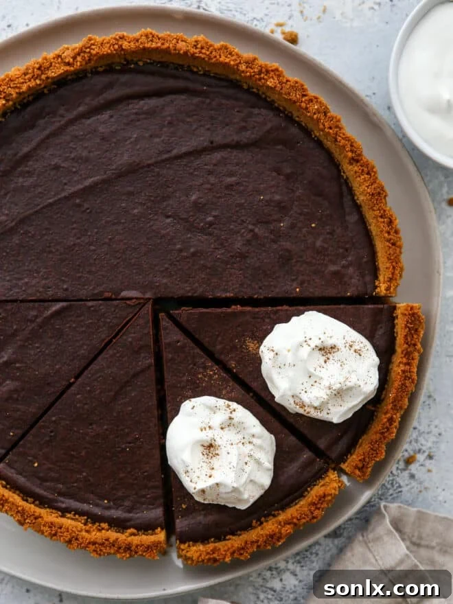 Sliced dark chocolate tart with whipped cream on the slices, ready to be served on a pristine white plate.