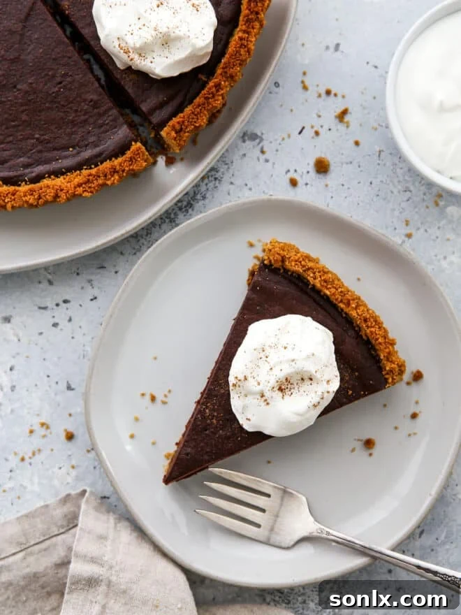 A perfectly portioned slice of dark chocolate tart adorned with whipped cream, artfully presented on a small white plate.