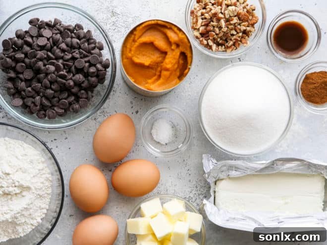 Assembled ingredients for baking pumpkin cheesecake swirl brownies including butter, chocolate, pumpkin puree, and cream cheese