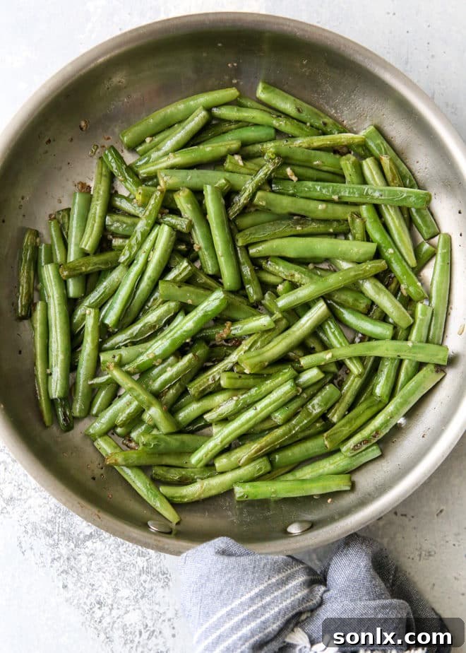 Cooked buttery garlic green beans garnished with fresh lemon wedges, ready to serve.