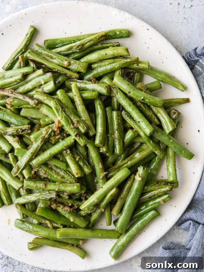 A vibrant pile of buttery garlic green beans in a white serving dish, garnished with parsley.