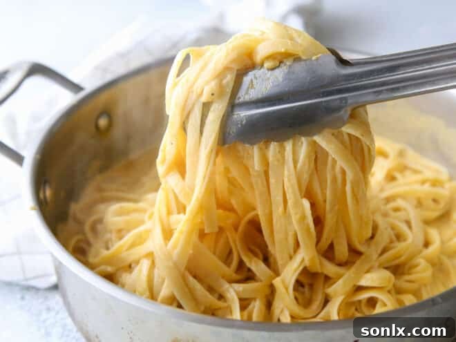 tossing pasta in pumpkin alfredo sauce in pot with tongs