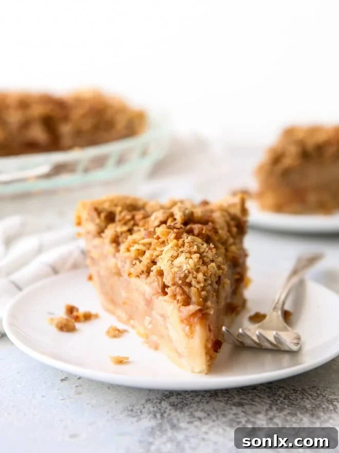 A perfectly baked slice of apple crumble pie with a golden, crisp topping, resting on a white plate.