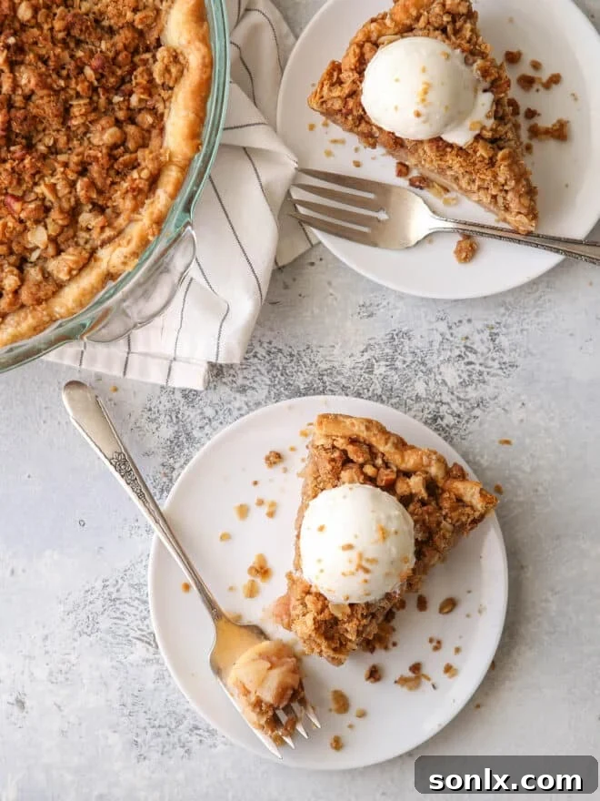 Several slices of apple crumble pie on plates, each topped with a scoop of vanilla ice cream, ready to be served.