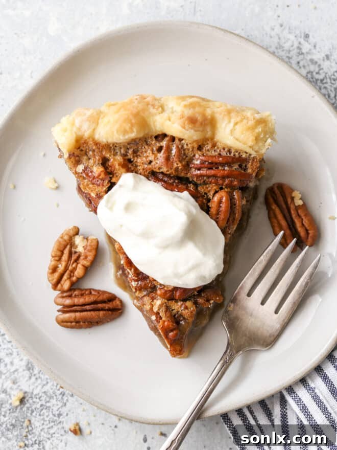 A perfectly portioned slice of classic pecan pie, topped with a generous swirl of fluffy whipped cream, presented on a white plate.