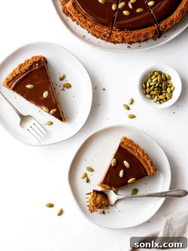 A delectable slice of chocolate pumpkin tart, highlighting the gingersnap crust, creamy pumpkin filling, and rich chocolate ganache topping. A full tart is visible in the background.