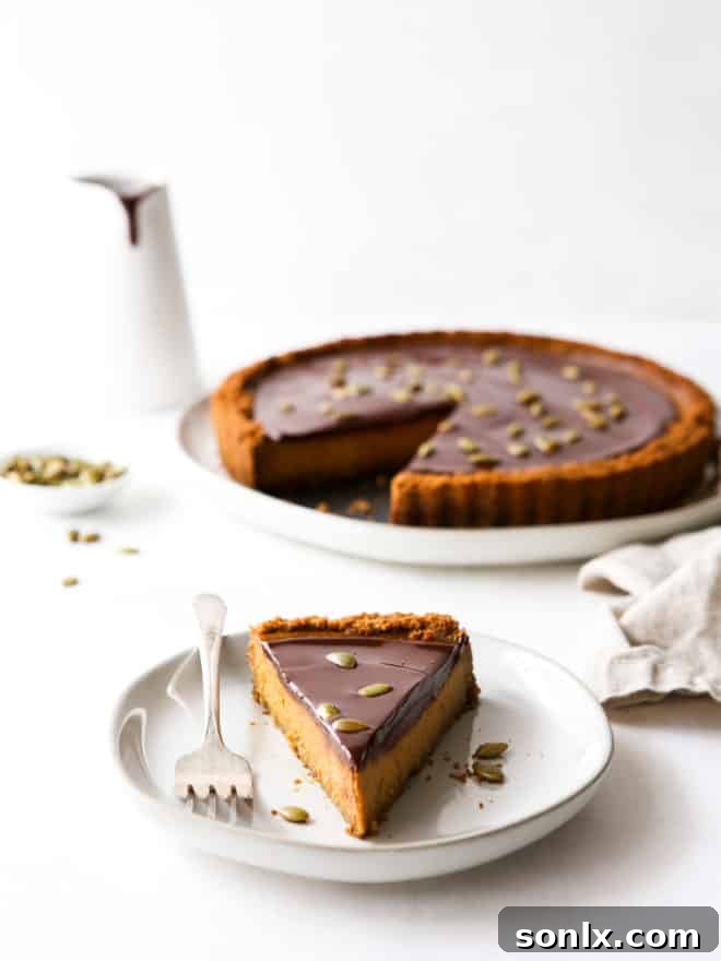 A slice of chocolate pumpkin tart on a white plate with a fork, with the full tart blurred in the background.