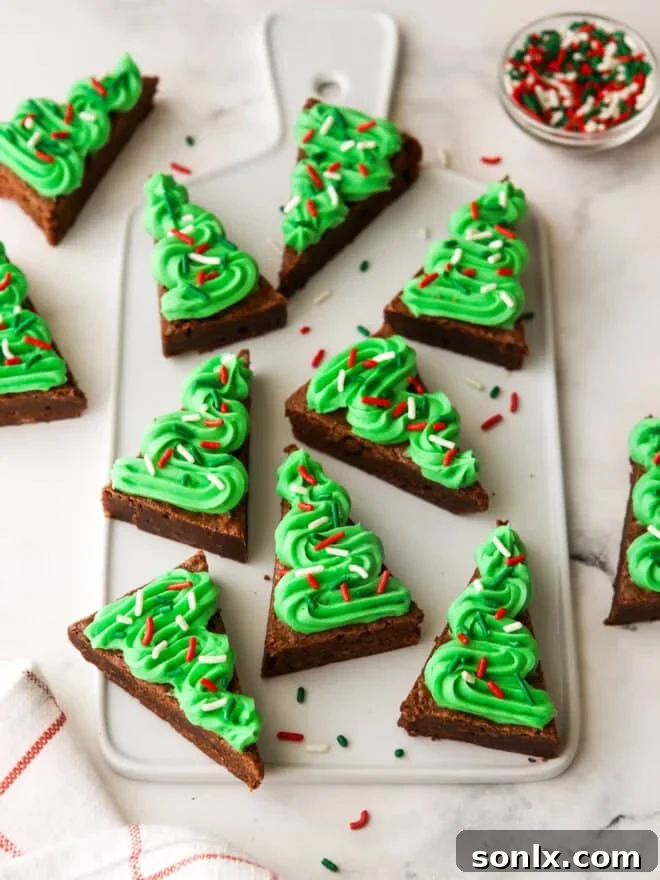 A festive tray of frosted brownie Christmas trees, each decorated with green frosting and colorful sprinkles, ready for a holiday party.