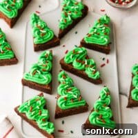 Frosted brownie cut-out cookies shaped like Christmas trees on a festive platter.