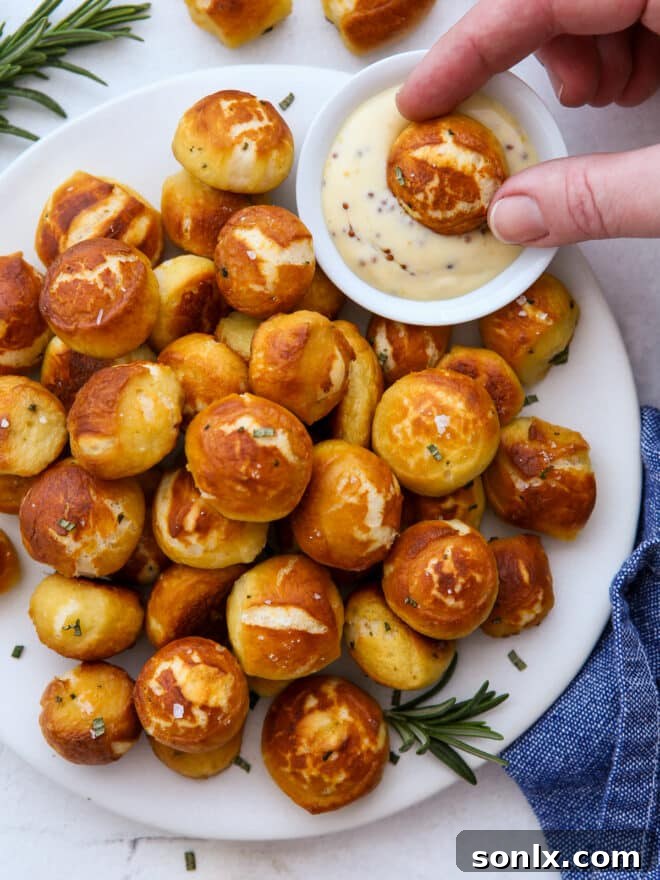 Close-up shot of cheddar rosemary pretzel bites on a white plate, ready to be dipped in honey mustard sauce.