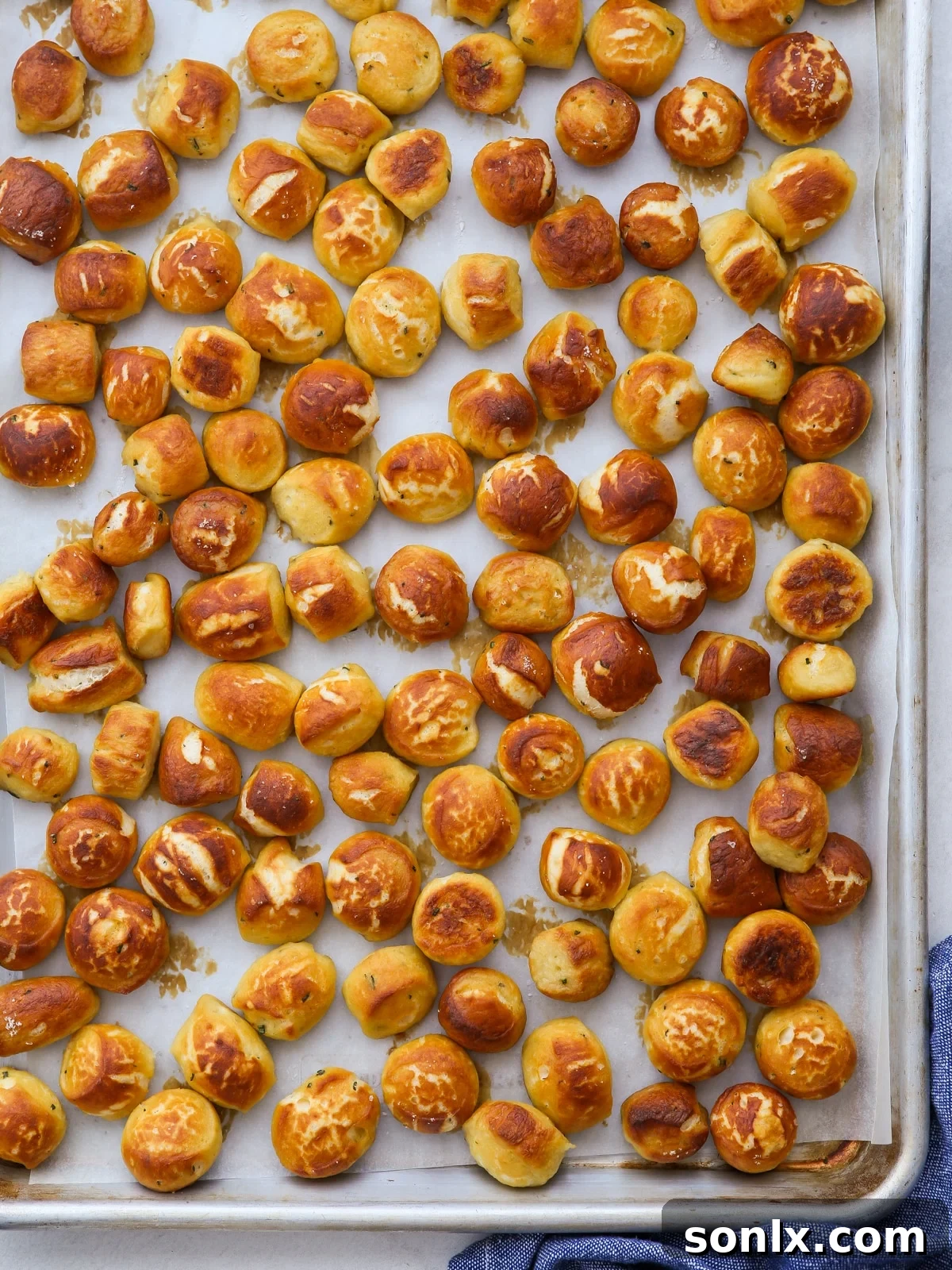 Freshly baked pretzel bites on a parchment-lined baking sheet, golden brown and sprinkled with coarse salt.