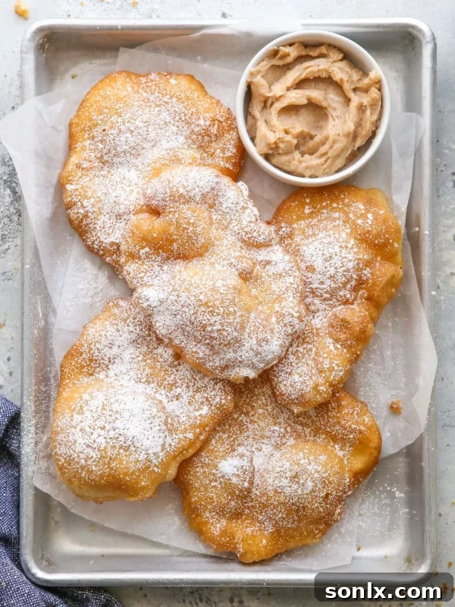 Warm, golden fry bread served on a rustic pan, with a small bowl of cinnamon honey butter next to it, inviting indulgence.