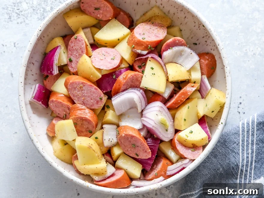 A spread of seven ingredients for sheet pan sausage and potatoes, neatly prepped on a cutting board.