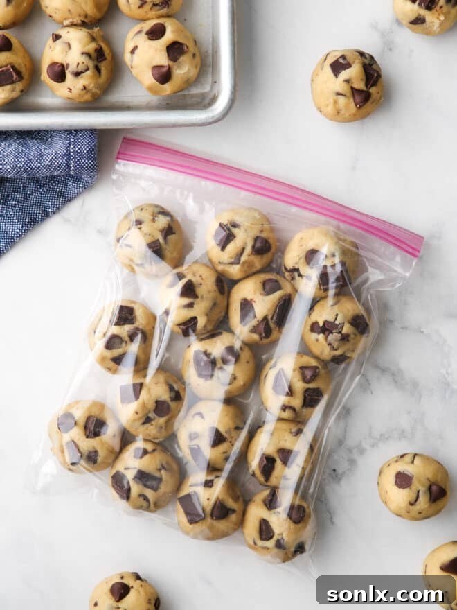 Rounds of chocolate chip cookie dough neatly packed in a ziplock bag, with a few extra portions on the side, ready for the freezer.