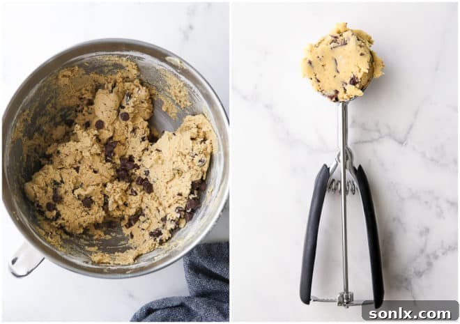 A large bowl of unbaked chocolate chip cookie dough, with a portion scooped out and ready to be formed into a ball.
