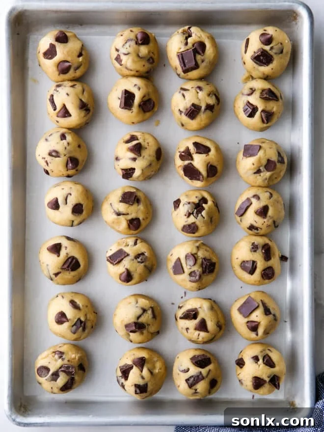 Several neatly portioned rounds of chocolate chip cookie dough arranged on a parchment-lined baking sheet, undergoing the flash-freezing process.