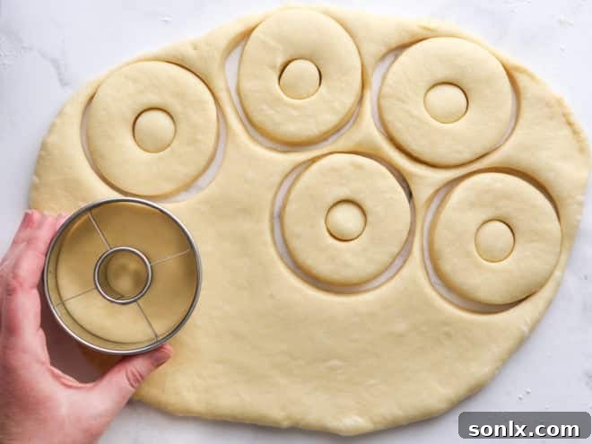 a pair of hands rolling out and cutting doughnut dough on a lightly floured surface with a round cutter