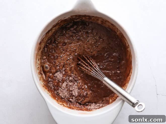 A close-up shot of a rich chocolate cupcake batter being mixed in a large bowl, highlighting the smooth texture and readiness for baking.