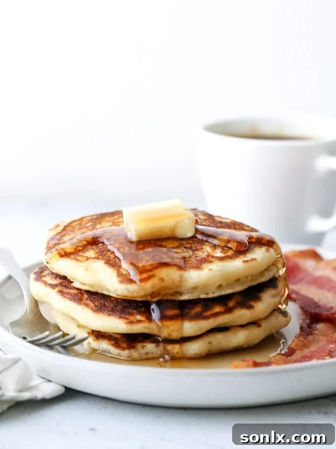 A stack of perfectly cooked buttermilk pancakes, golden brown and fluffy, drizzled with syrup and ready to be served.