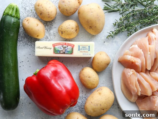 Essential ingredients laid out for preparing chicken and veggie tin foil dinners, including chicken, potatoes, bell pepper, zucchini, butter, and fresh herbs.