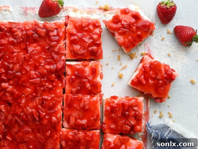 Two pieces of no-bake strawberry cheesecake bars, showcasing the distinct layers of crust, filling, and strawberry topping